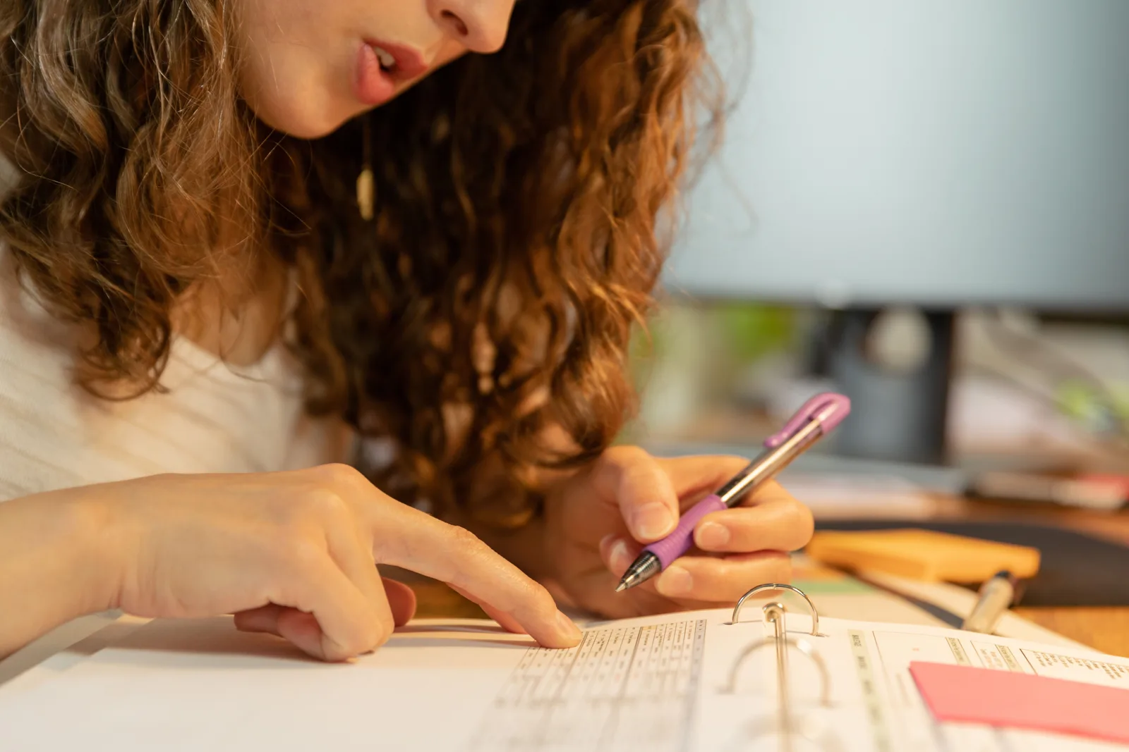 Focused woman pointing and writing on paper in binder with a purple pen. Translation agency expansion: choices, constraints and risks